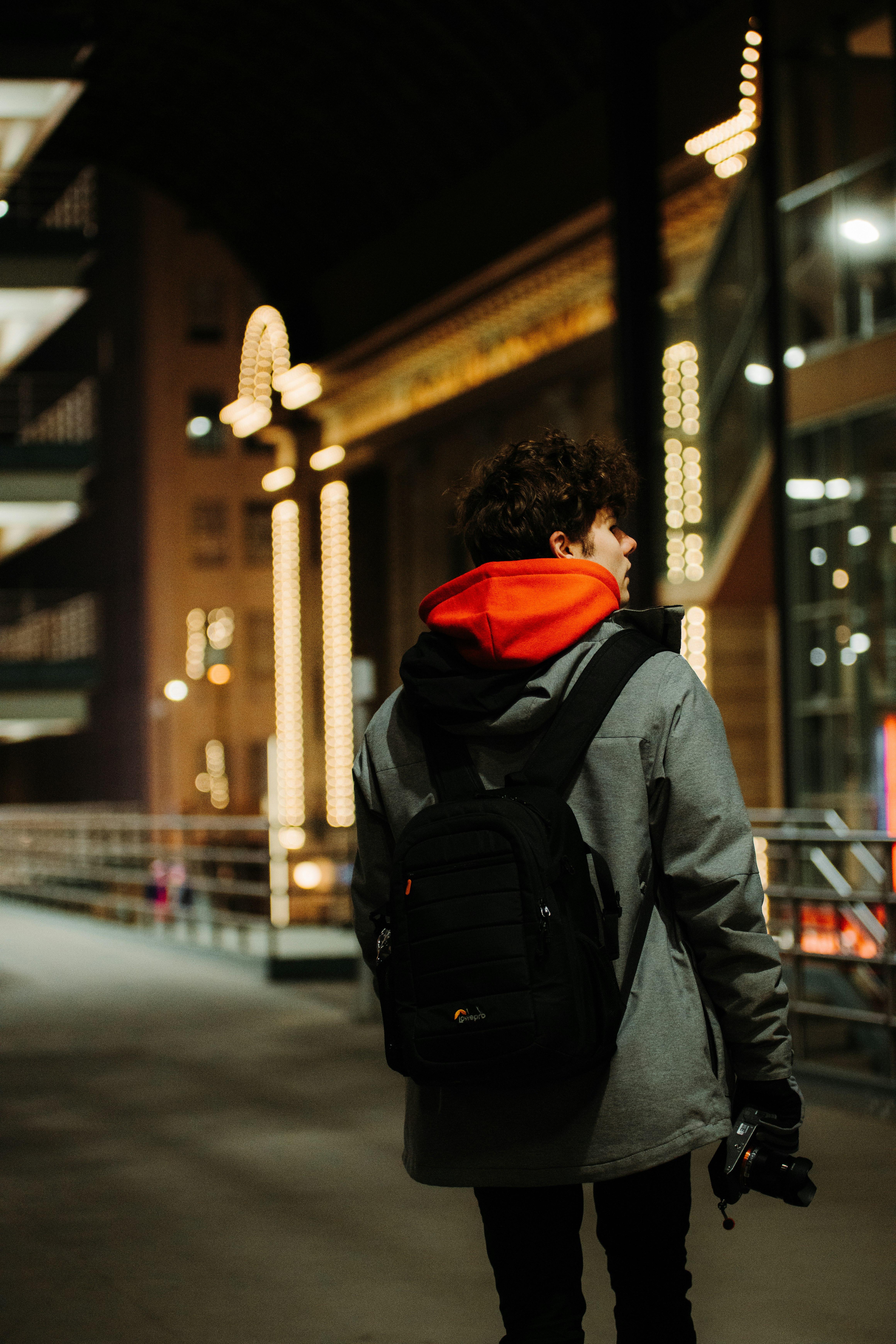 person in black and orange hoodie and black backpack walking on sidewalk during daytime